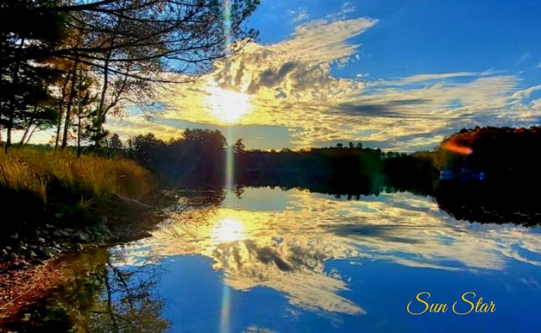 Sun overlooking lake casting a sunbeam into the water